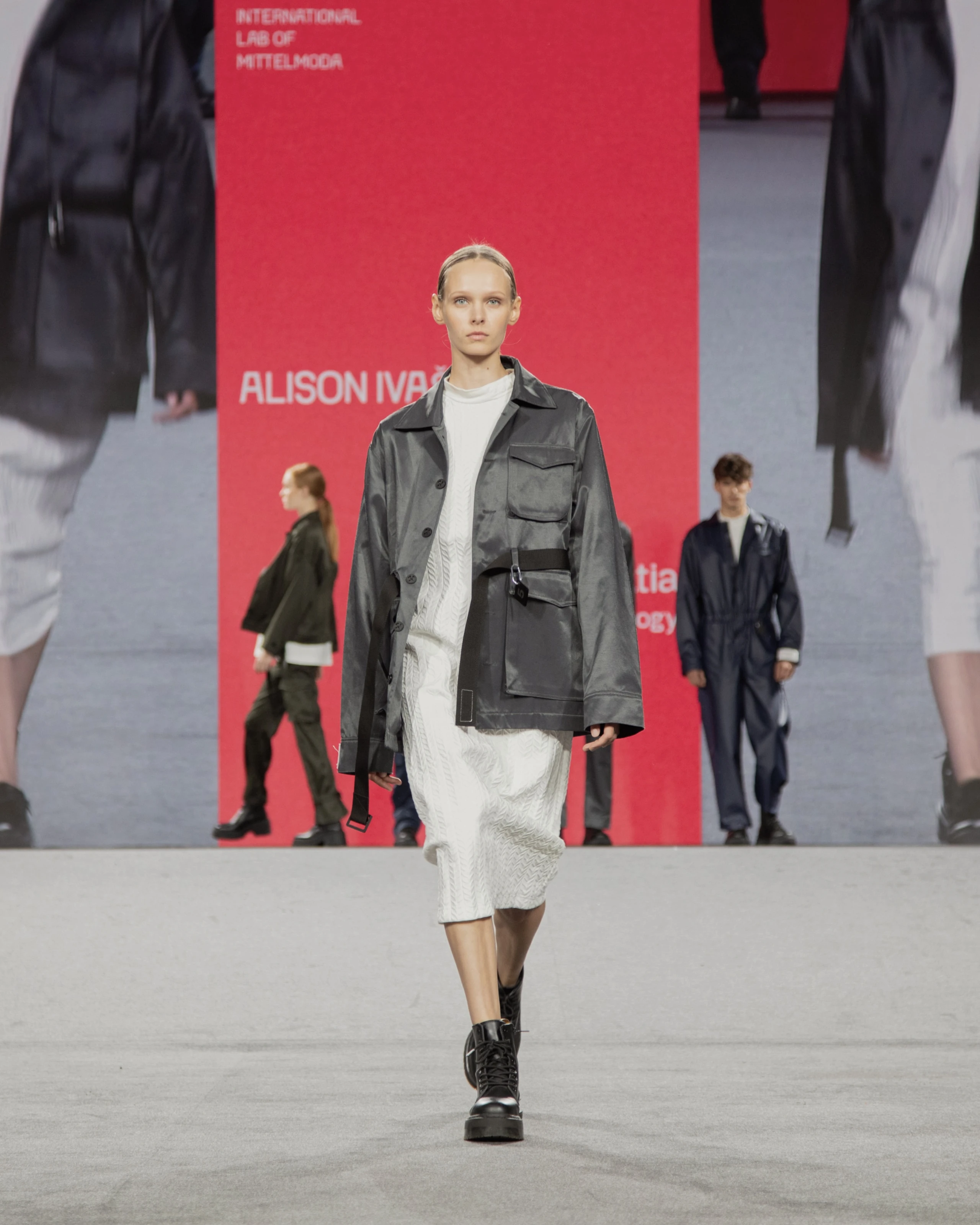 Model wearing gray jacket and white dress from KOVARI collection on Mittelmoda show.