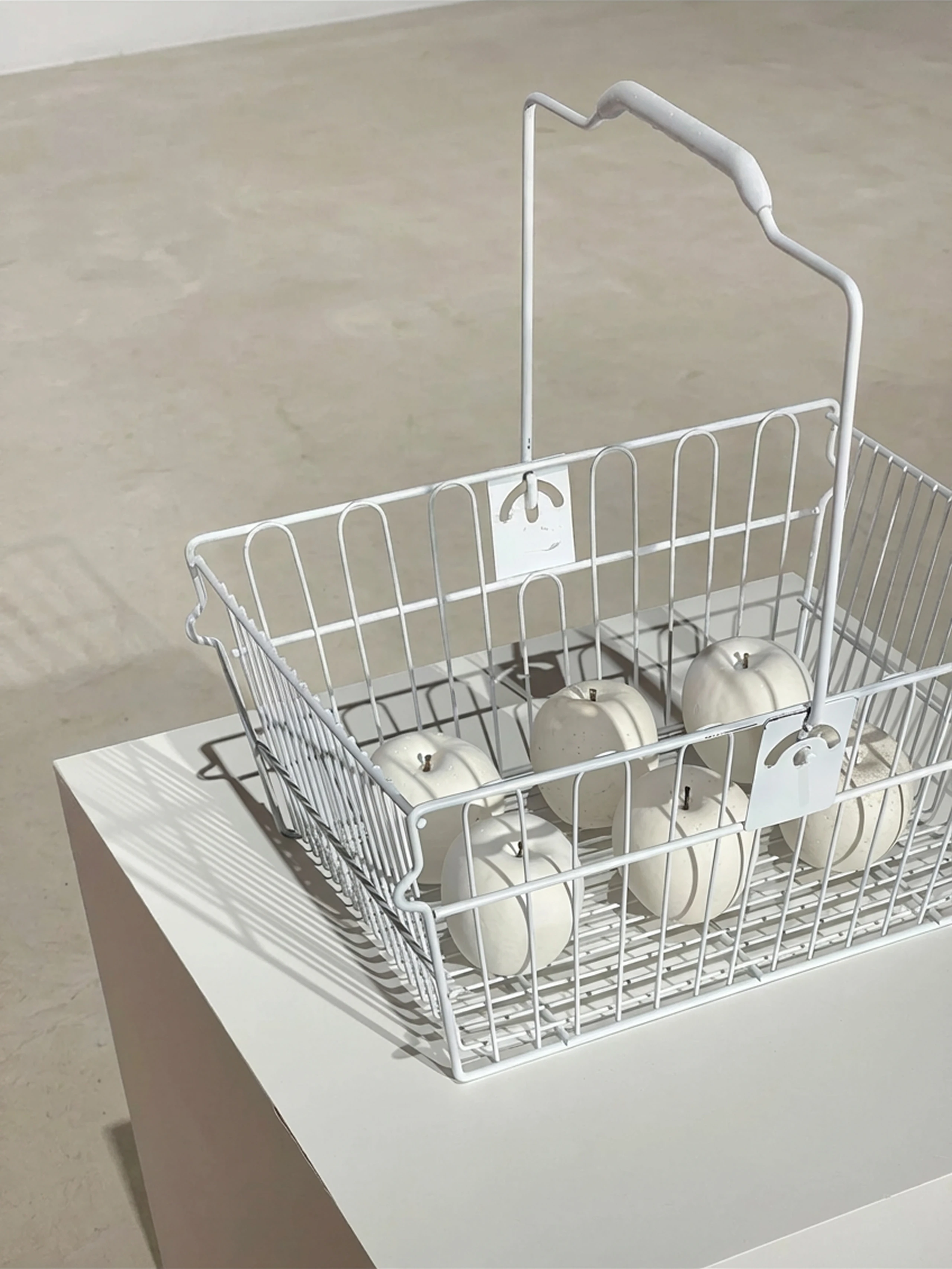 Art installation showing six white plaster apples placed inside a white shopping cart.